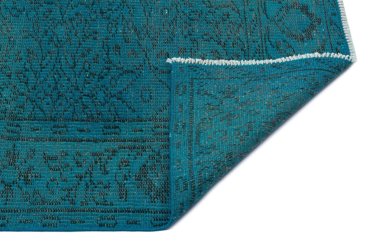 Teal rug with a dark grey traditional floral pattern, shown with a corner folded over to reveal the underside.