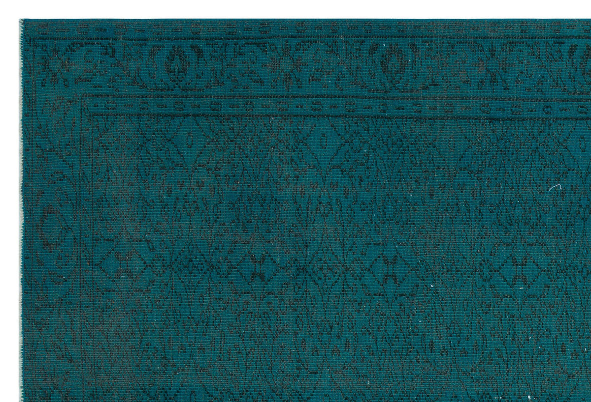 Teal rug with a dark, intricate geometric diamond pattern and a decorative border.