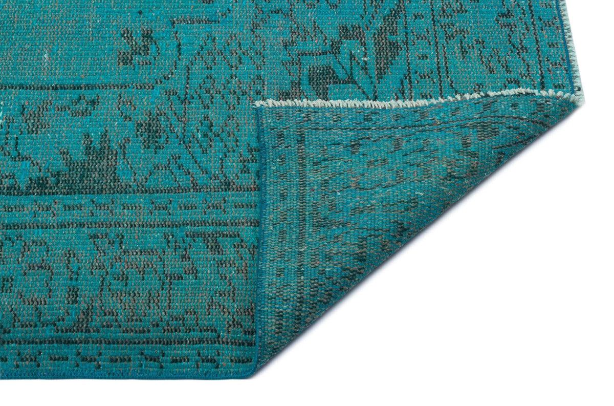 Teal and charcoal distressed rug with a traditional medallion pattern, shown with a corner folded over on a white background.