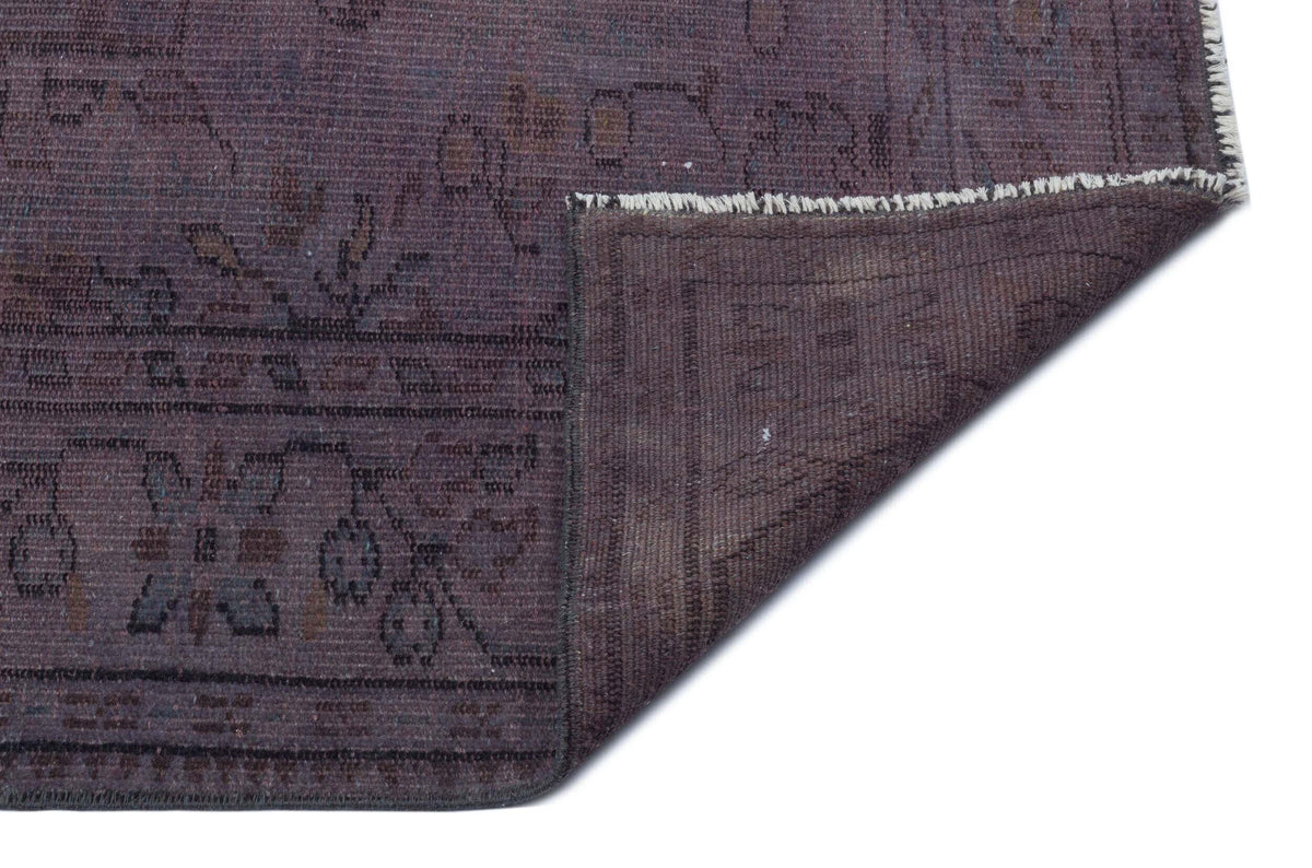 Dark purple distressed rug with a faded floral pattern and a folded corner showing the woven backing.