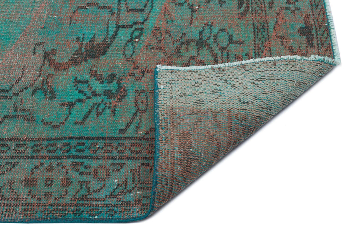 Teal and brown distressed vintage-style rug with a floral medallion pattern, shown with a corner folded over.
