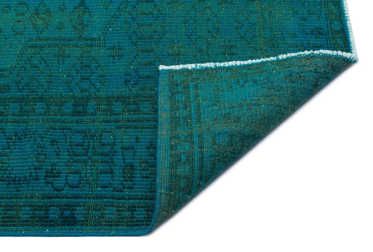 Teal rug with a dark geometric pattern and a folded corner revealing the underside, isolated on a white background.