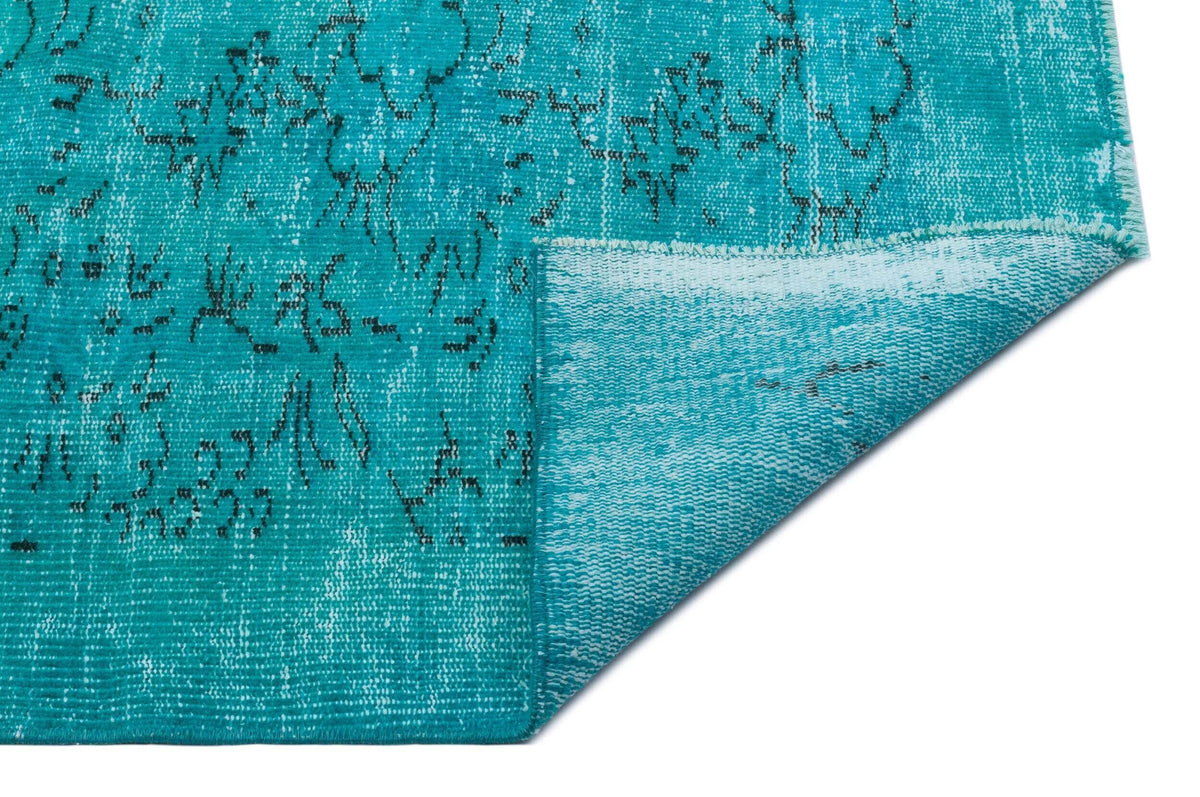 Turquoise distressed rug with a faded black floral pattern, shown with a folded corner on a white background.