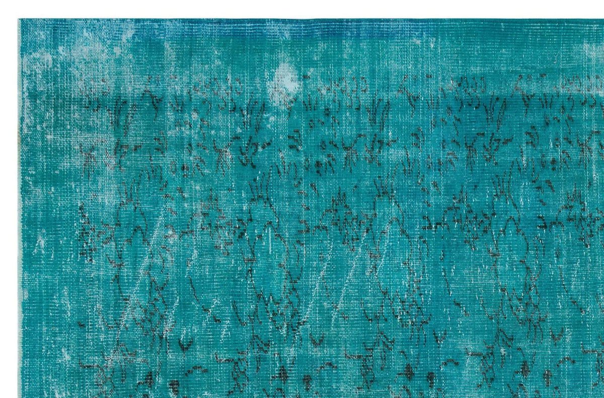 Teal distressed rug with a faded black floral pattern and white worn-out texture.
