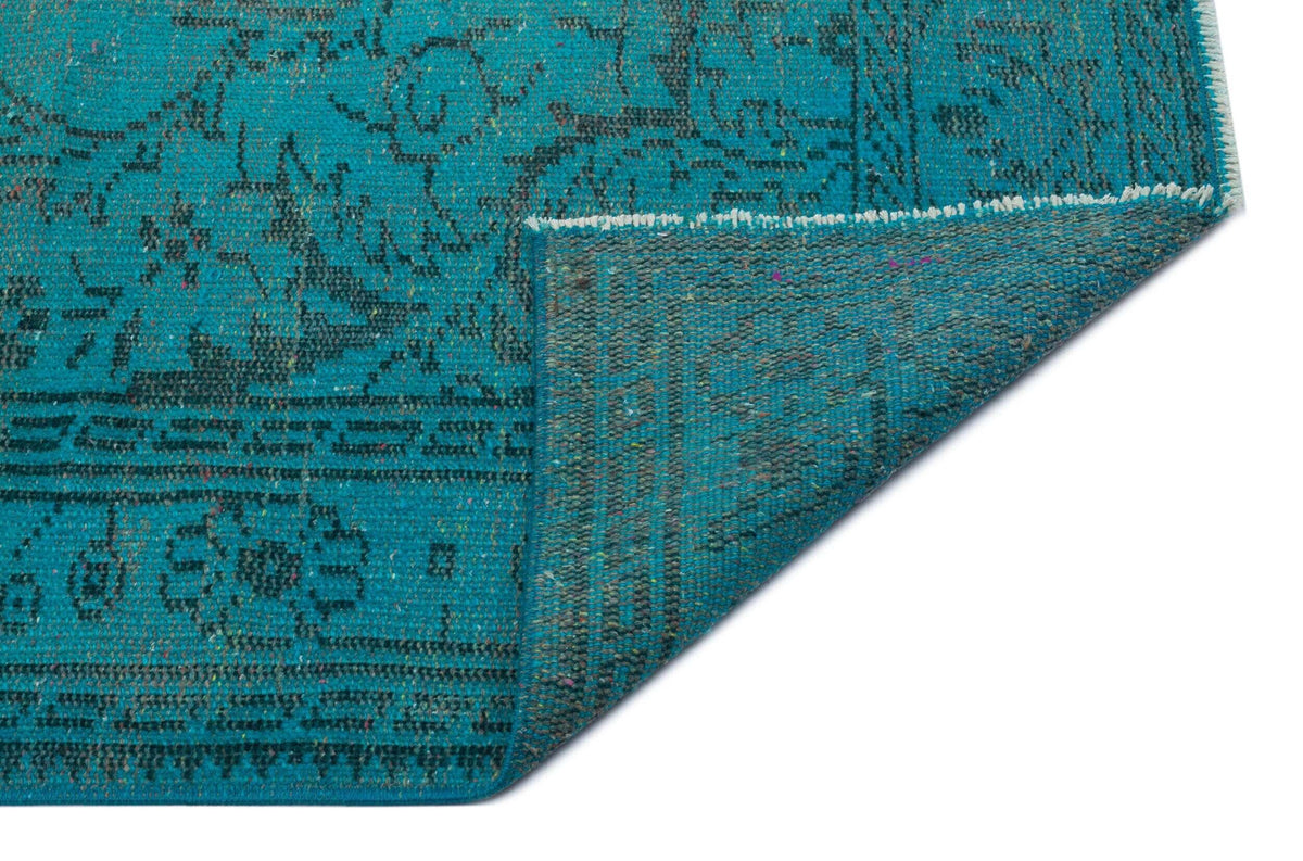 Teal rug with a distressed black traditional floral pattern, shown with a corner folded over on a white background.