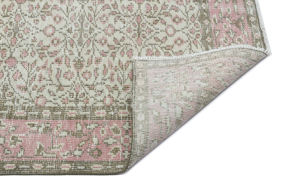 Cream, pink, and taupe floral medallion rug with a folded corner revealing the woven backing.