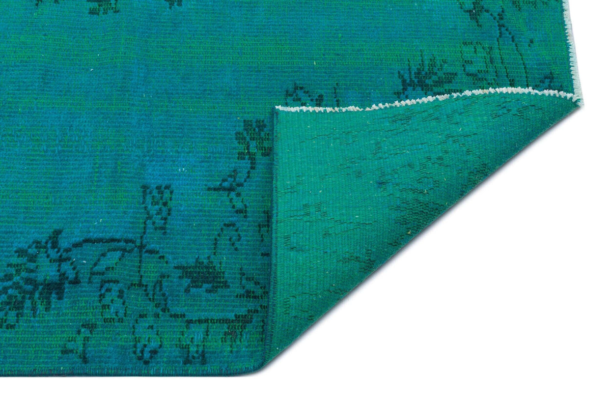Teal rug with a black floral pattern and a folded corner revealing the textured underside on a white background.