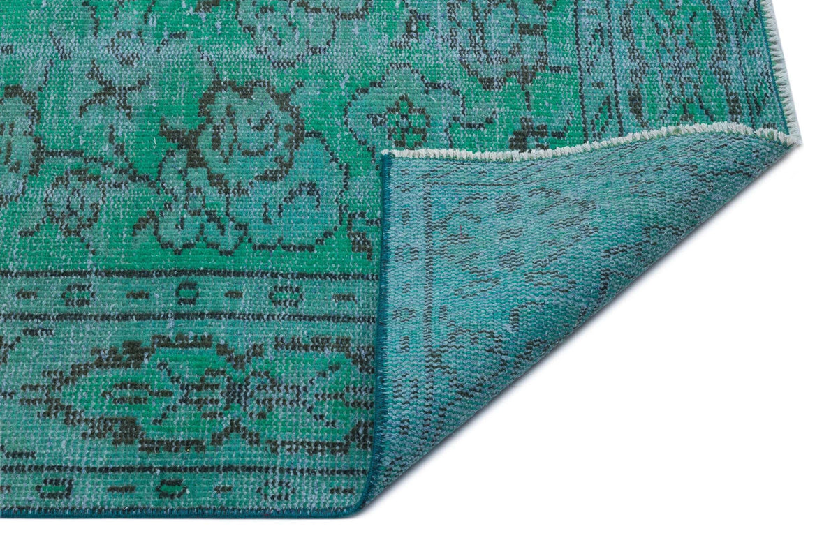 Emerald green and teal distressed rug with a dark grey floral medallion pattern, shown with a folded corner.