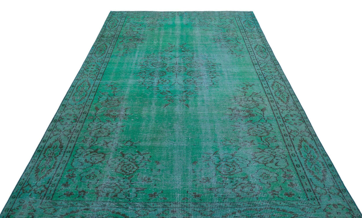 Emerald green vintage-style rug with a distressed, faded black floral medallion pattern and a decorative border.