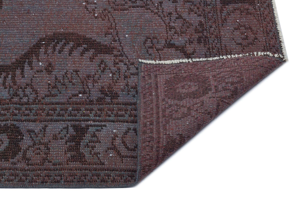 Deep plum and charcoal distressed rug with a traditional medallion pattern, shown with a corner folded over.