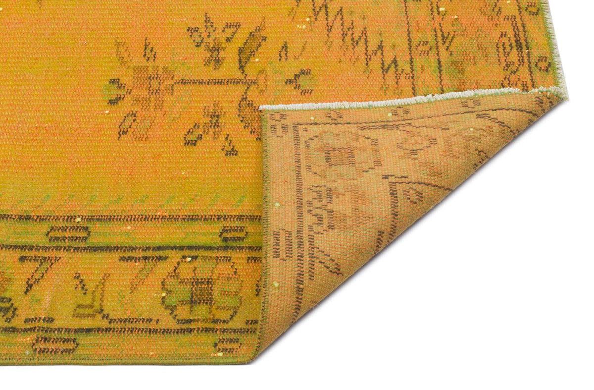 Mustard yellow vintage-style rug with a faded floral pattern and a folded corner showing the underside.