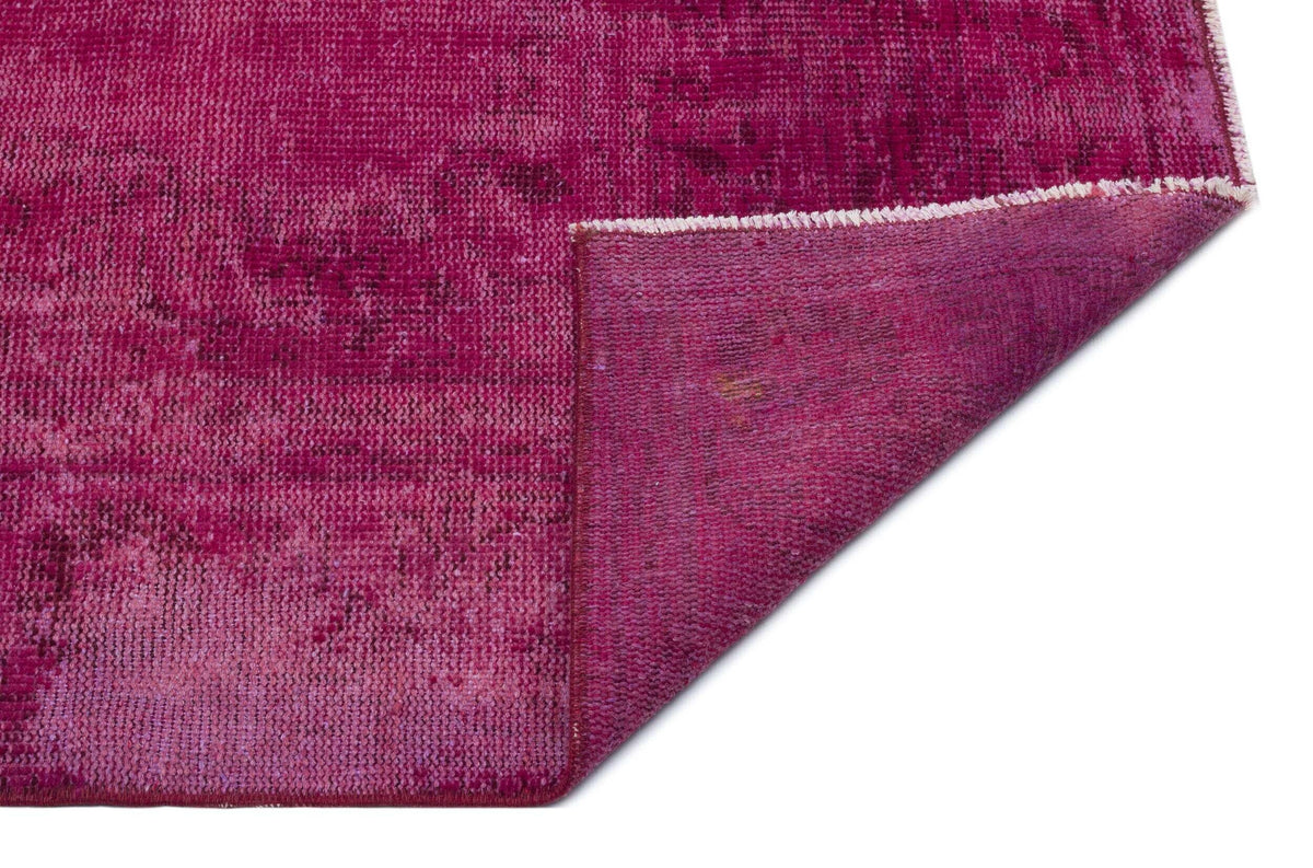 Magenta distressed overdyed rug with a folded corner revealing the woven backing.