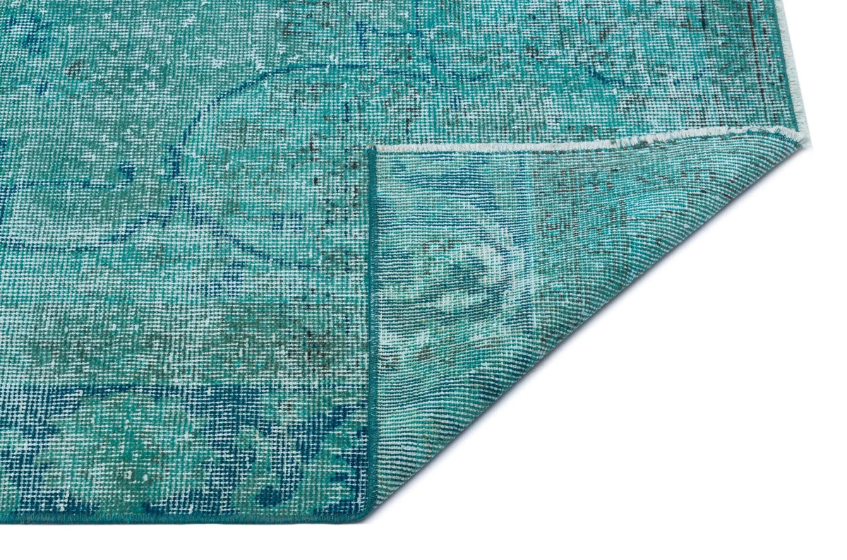 Teal and blue distressed rug with a faded traditional medallion pattern, shown with a corner folded over.