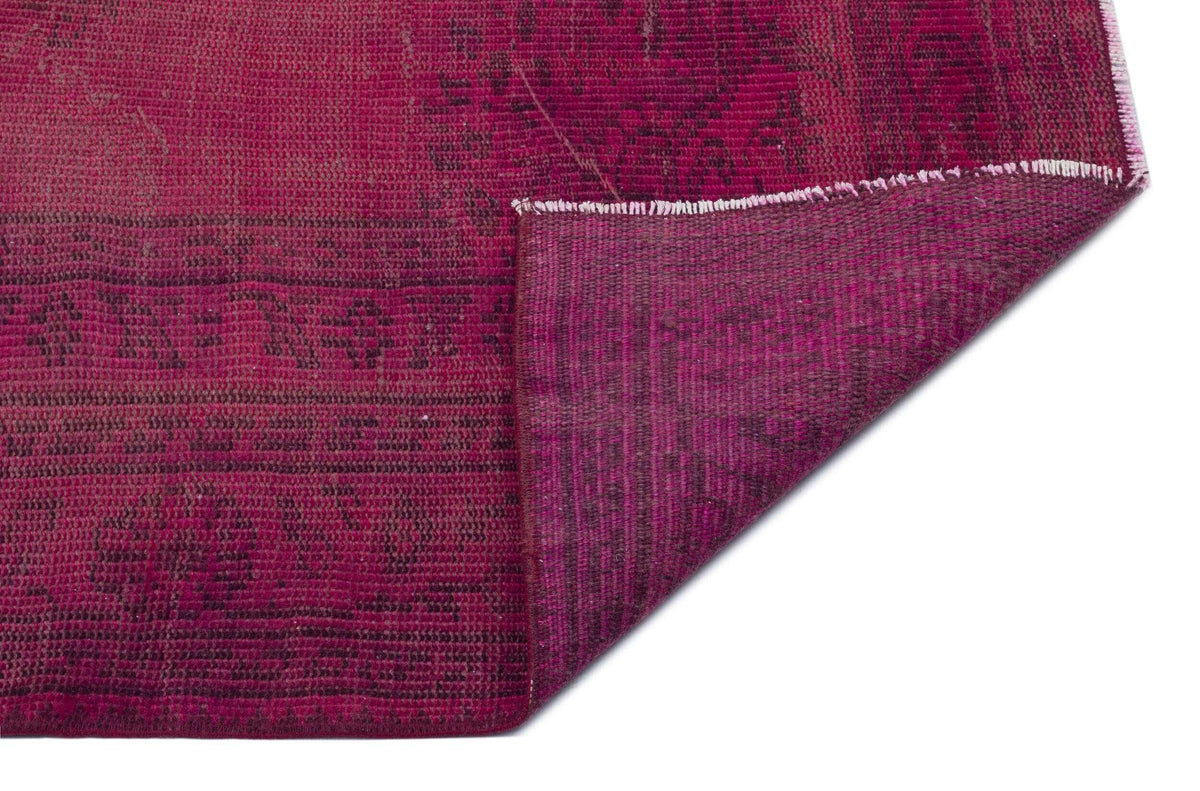 Magenta distressed rug with a dark, faded geometric pattern and a folded corner showing the underside texture.