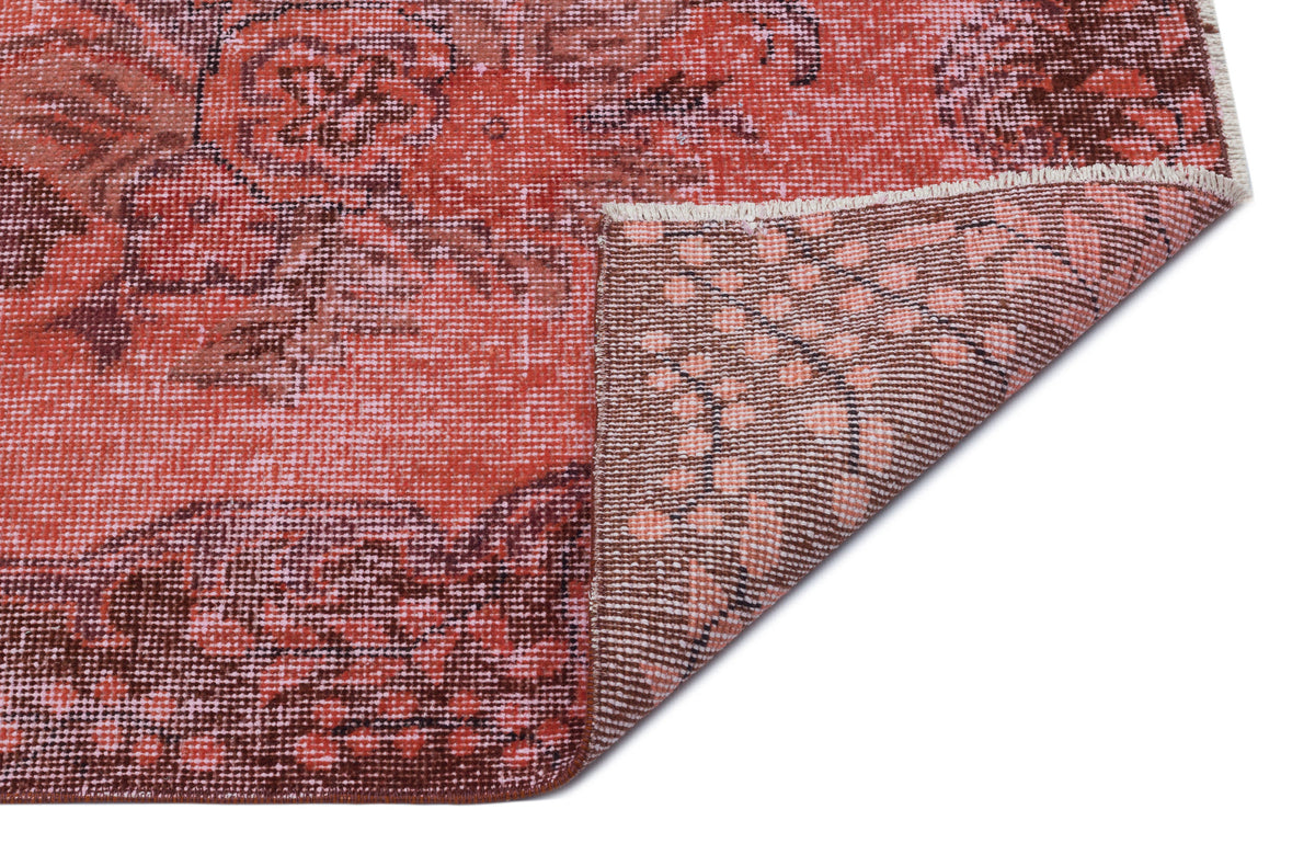 Distressed coral and brown rug with a floral medallion pattern, showing the underside corner on a white background.