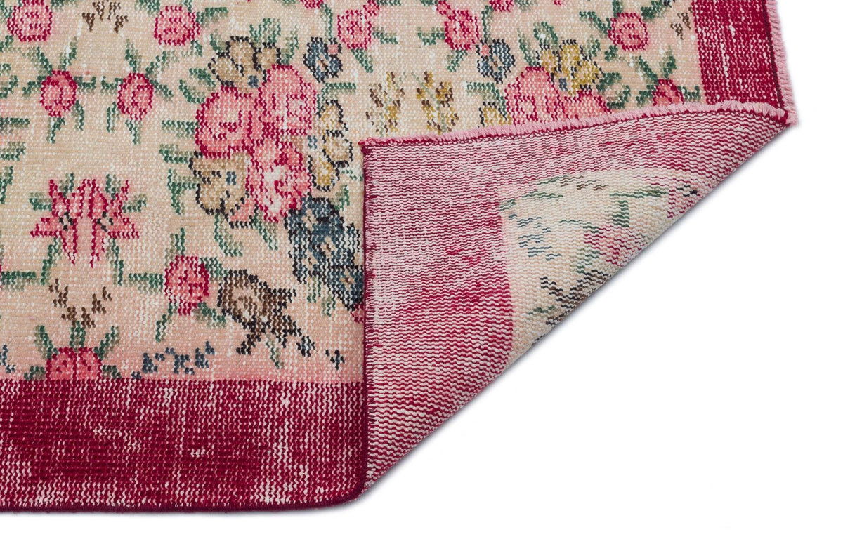 Beige rug with a pink floral pattern and a wide magenta border, shown with a corner folded over on a white background.