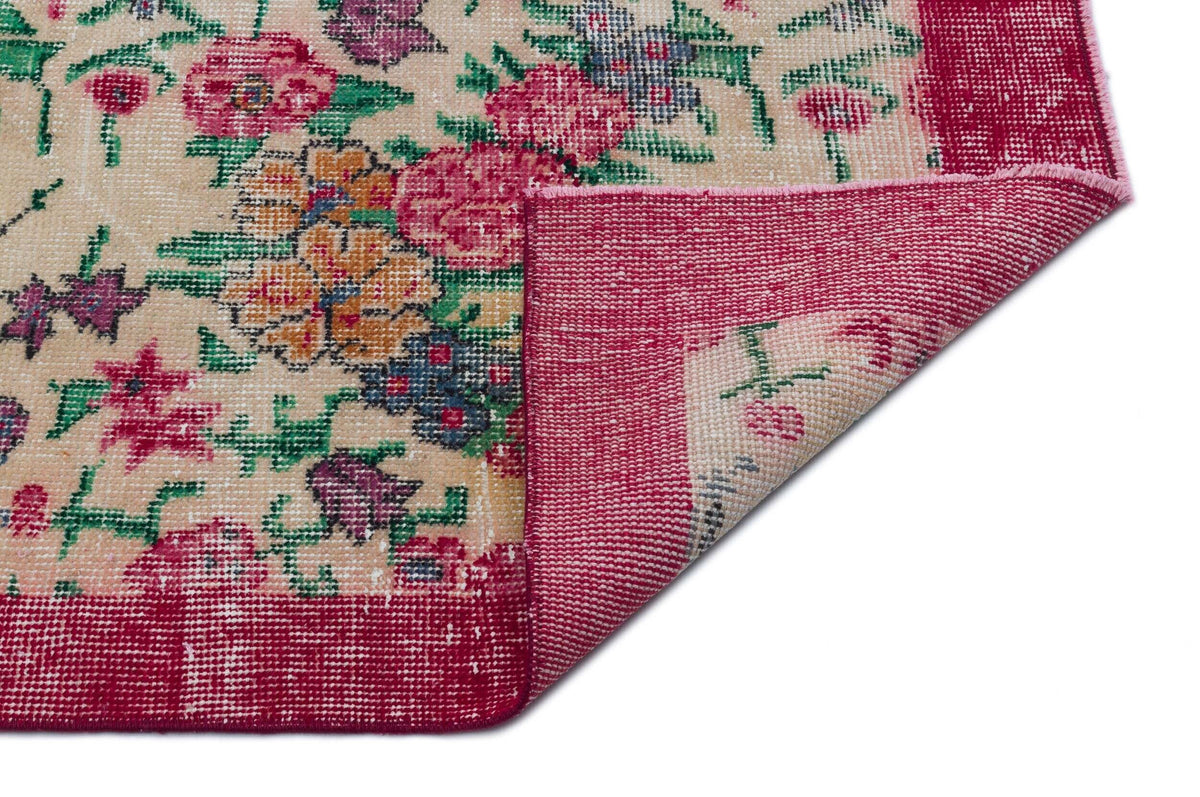 Beige rug with a multi-colored floral pattern and a wide magenta border, shown with a corner folded over.