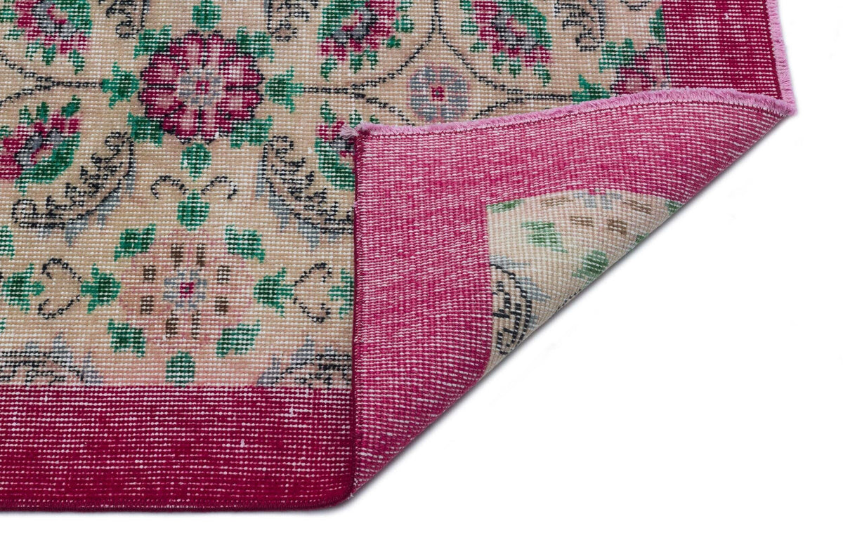 Beige rug with a floral medallion pattern in magenta and green, featuring a wide magenta border and a folded corner.