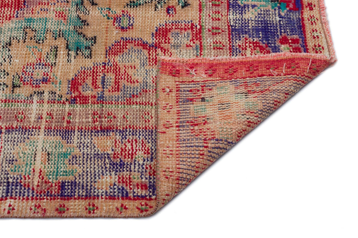 Distressed multi-colored rug with a traditional floral pattern in red, blue, and teal on a tan background.
