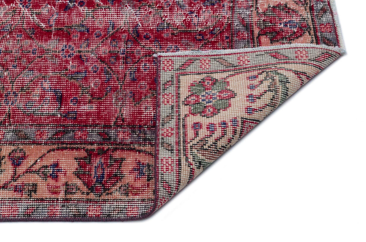Distressed red and cream traditional rug with a floral medallion pattern, shown with a corner folded over.
