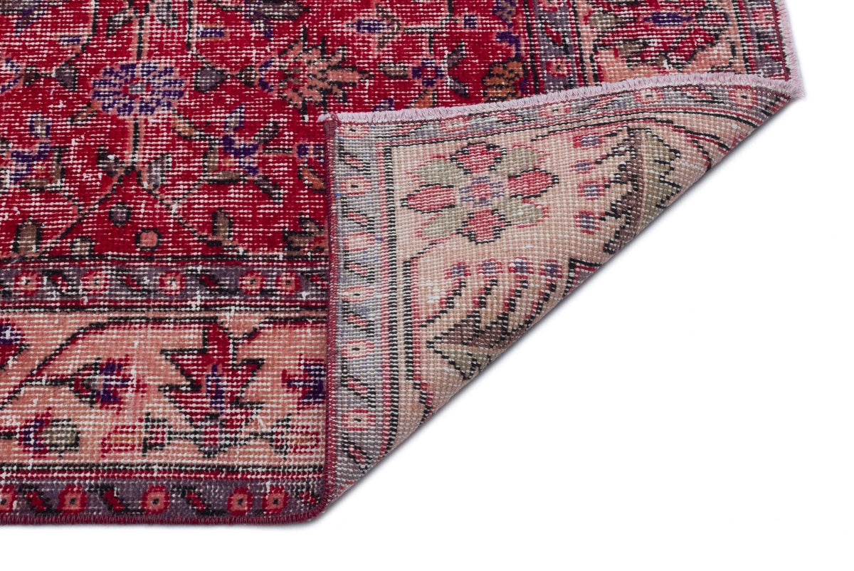 Red and beige vintage-style rug with a floral medallion pattern, showing a folded corner on a white background.