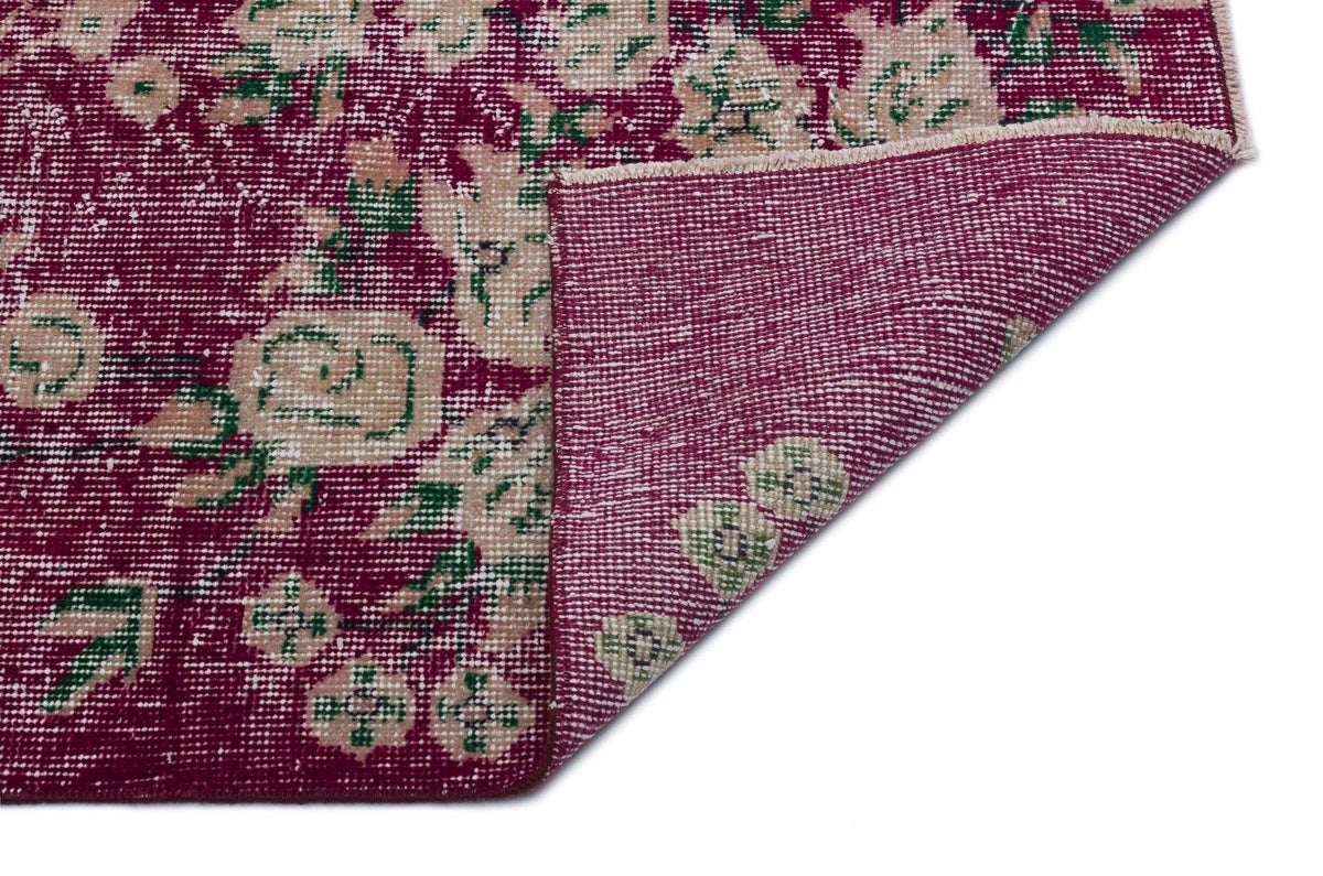 Magenta and cream floral rug with a distressed finish, shown with a corner folded over to reveal the backing.