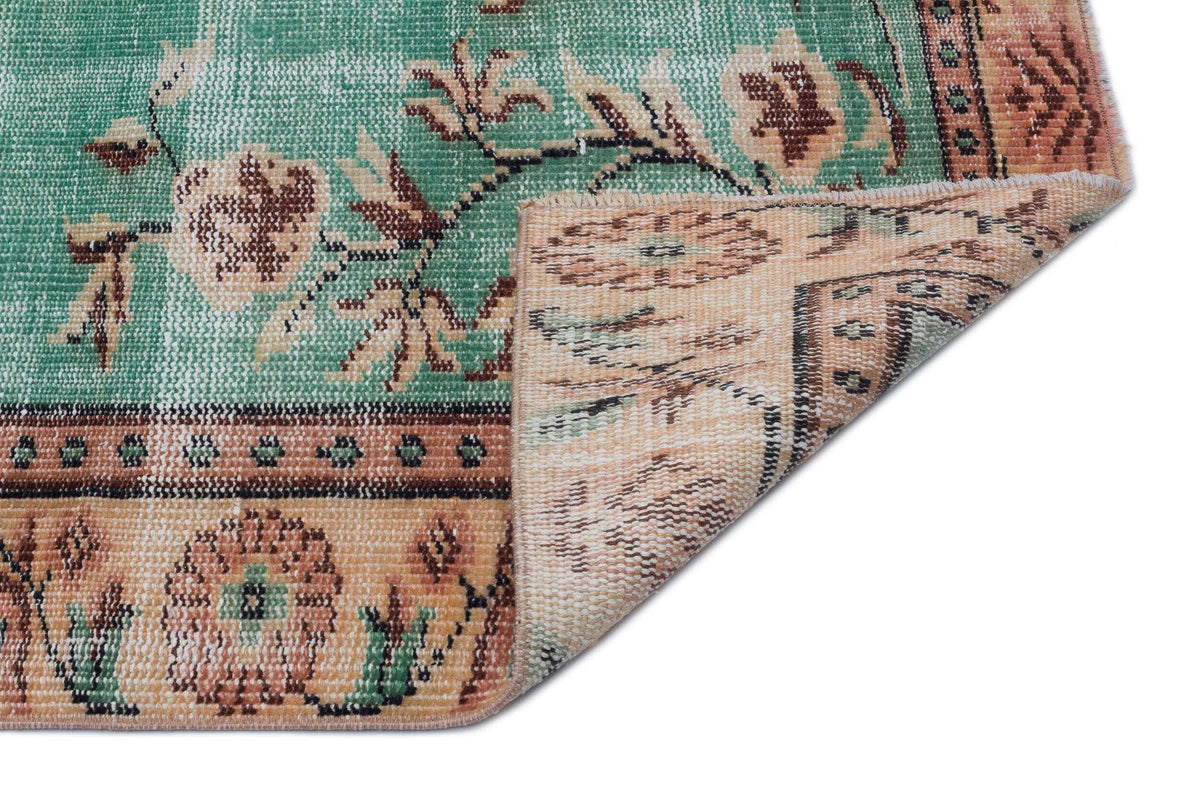 Green and beige vintage-style rug with a floral pattern and a folded corner revealing the woven backing.