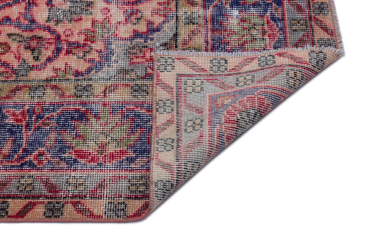 Distressed traditional rug with a floral medallion pattern in red, blue, and beige, shown with a folded corner.