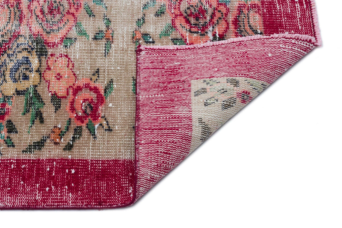 Beige and magenta floral rug with a distressed finish, showing a folded corner revealing the woven backing.