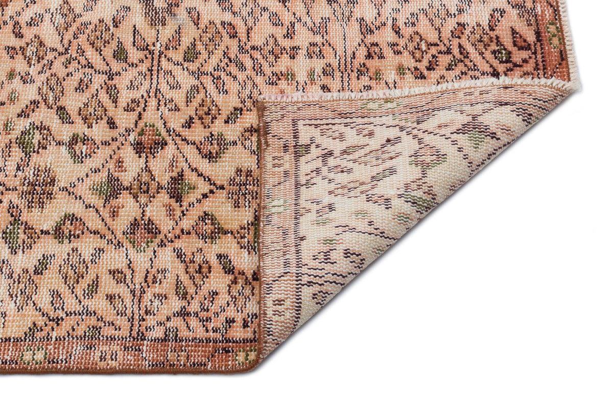 Peach and brown rug with a floral medallion pattern, shown with a corner folded to reveal the woven backing.
