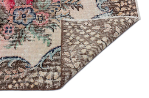 Load image 1 in gallery view. Beige rug with a floral medallion pattern in pink, blue, and green, showing a folded corner on a white background.