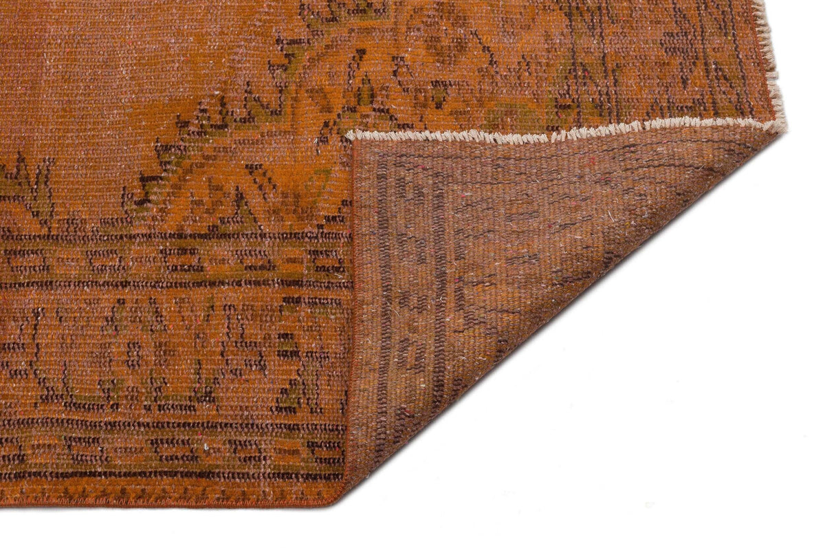 Burnt orange vintage-style rug with a distressed traditional pattern and a folded corner showing the woven backing.