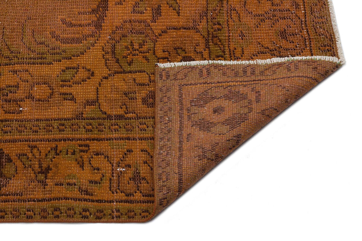 Rust and brown vintage-style rug with a traditional floral medallion pattern and a folded corner on a white background.