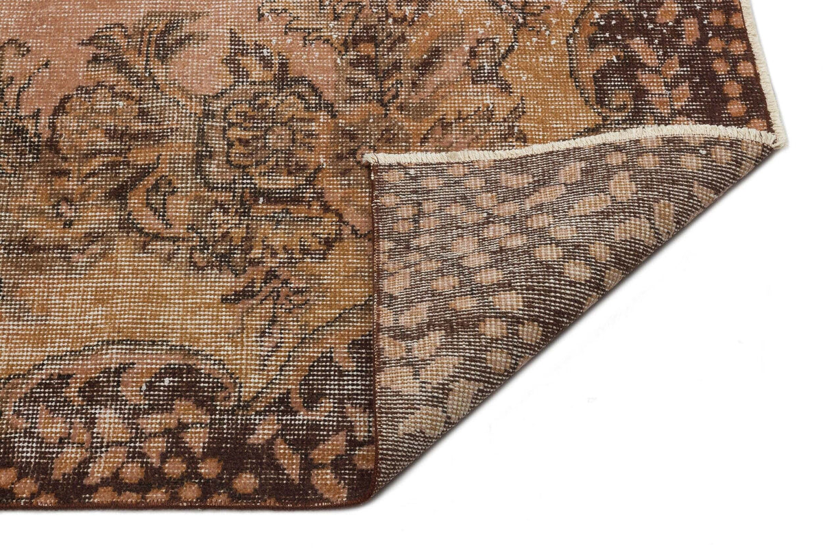 Distressed brown and tan rug with a floral medallion pattern, shown with a corner folded over on a white background.