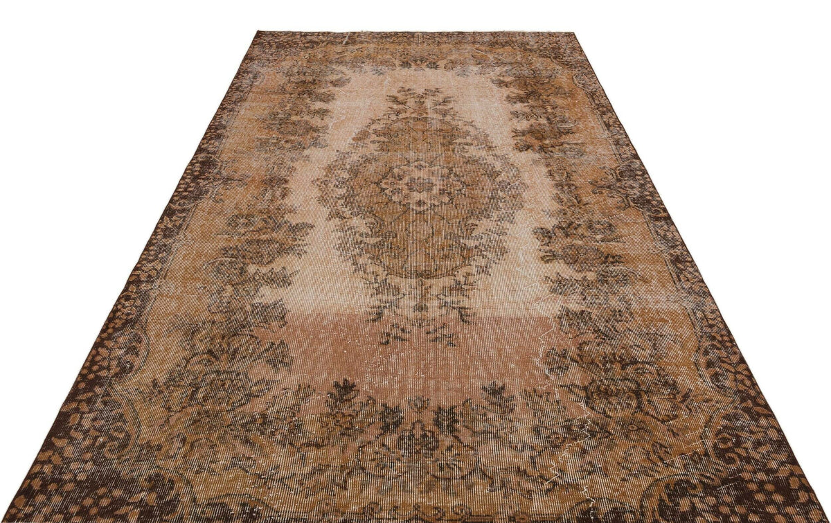 Distressed brown and beige vintage-style rug with a central floral medallion and ornate border on a white background.