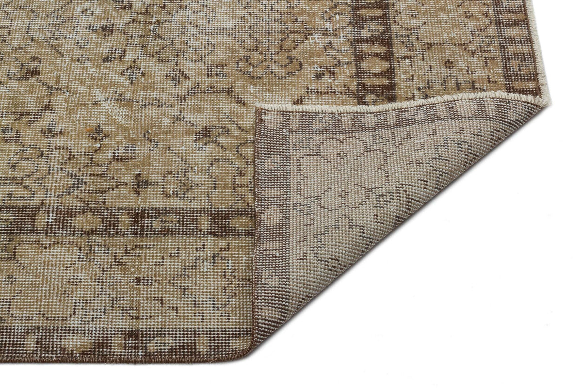 Tan and brown distressed traditional rug with a floral medallion pattern, shown with a corner folded over.