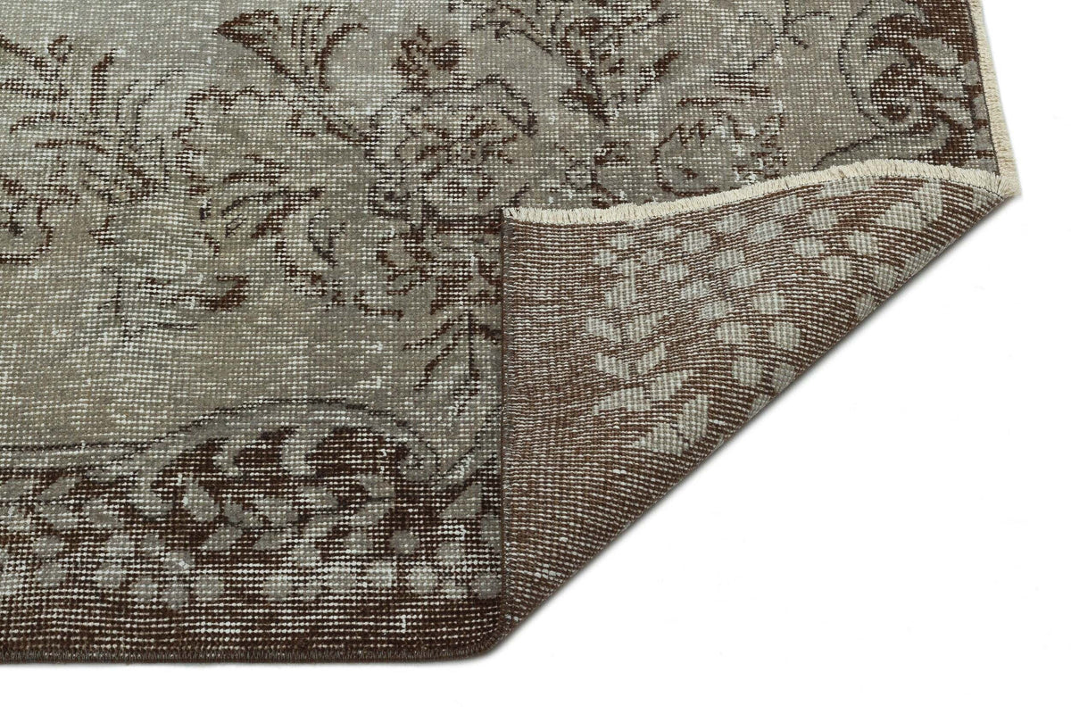 Taupe and brown distressed rug with a floral medallion pattern, shown with a corner folded to reveal the woven backing.