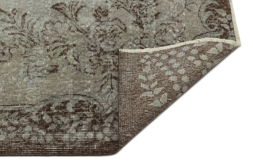 Load image 1 in gallery view. Taupe and brown distressed rug with a floral medallion pattern, shown with a corner folded to reveal the woven backing.