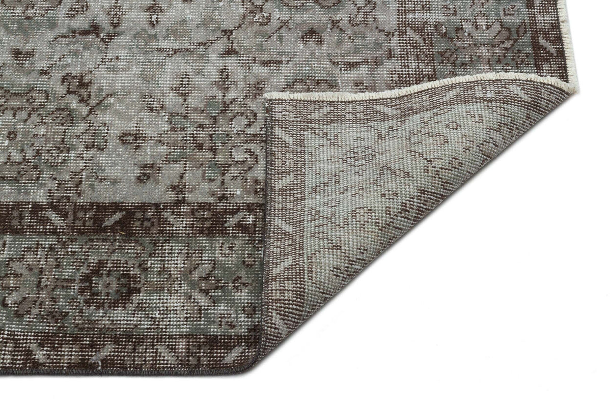 Grey and brown distressed traditional rug with a floral medallion pattern, shown with a corner folded over.