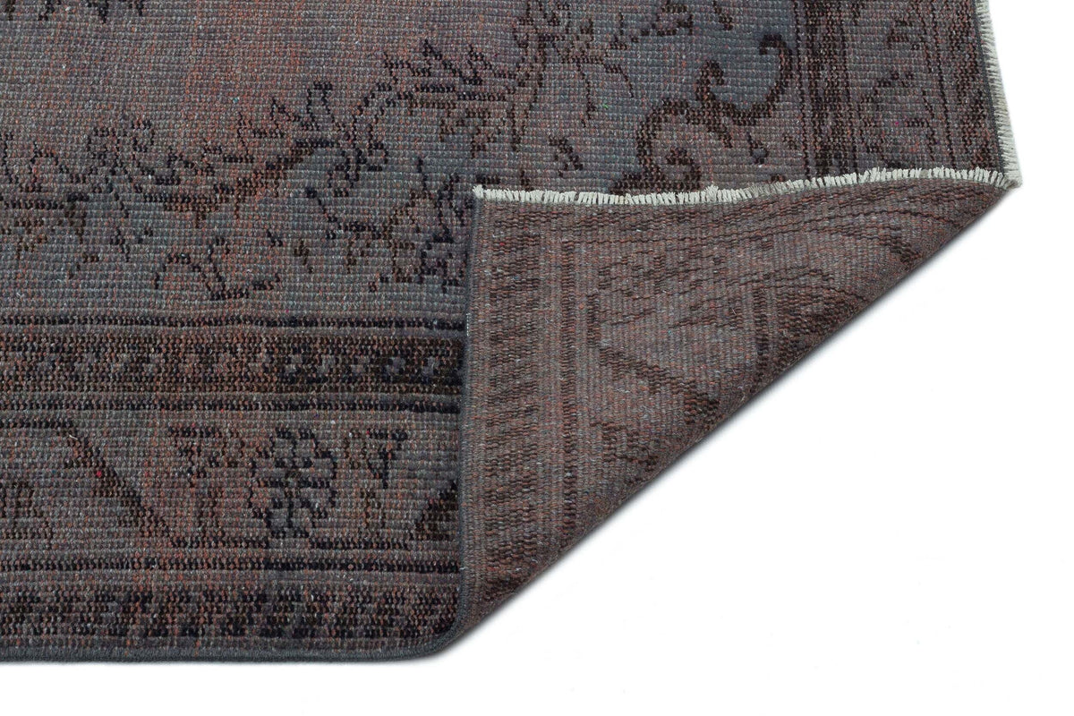 Charcoal and brown distressed rug with a traditional floral medallion pattern, shown with a folded corner.