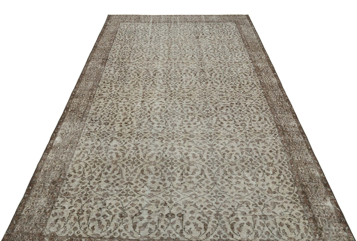 Brown and beige vintage-style rug with an intricate distressed floral pattern and a wide decorative border.