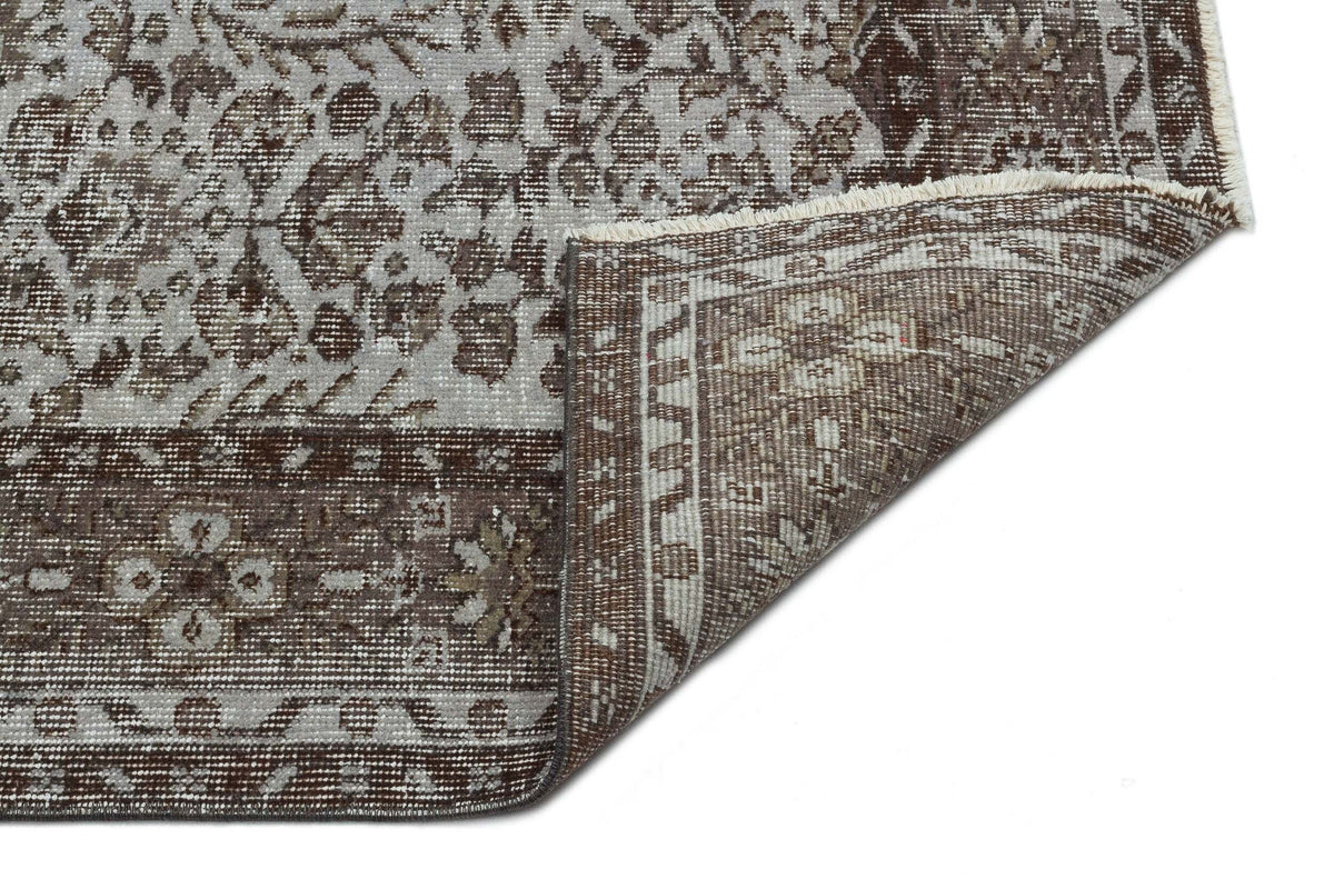 Brown and grey vintage-style rug with a floral medallion pattern and a folded corner showing the woven backing.