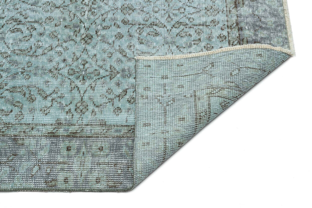 Light blue and grey distressed rug with a traditional floral medallion pattern, shown with a corner folded over.