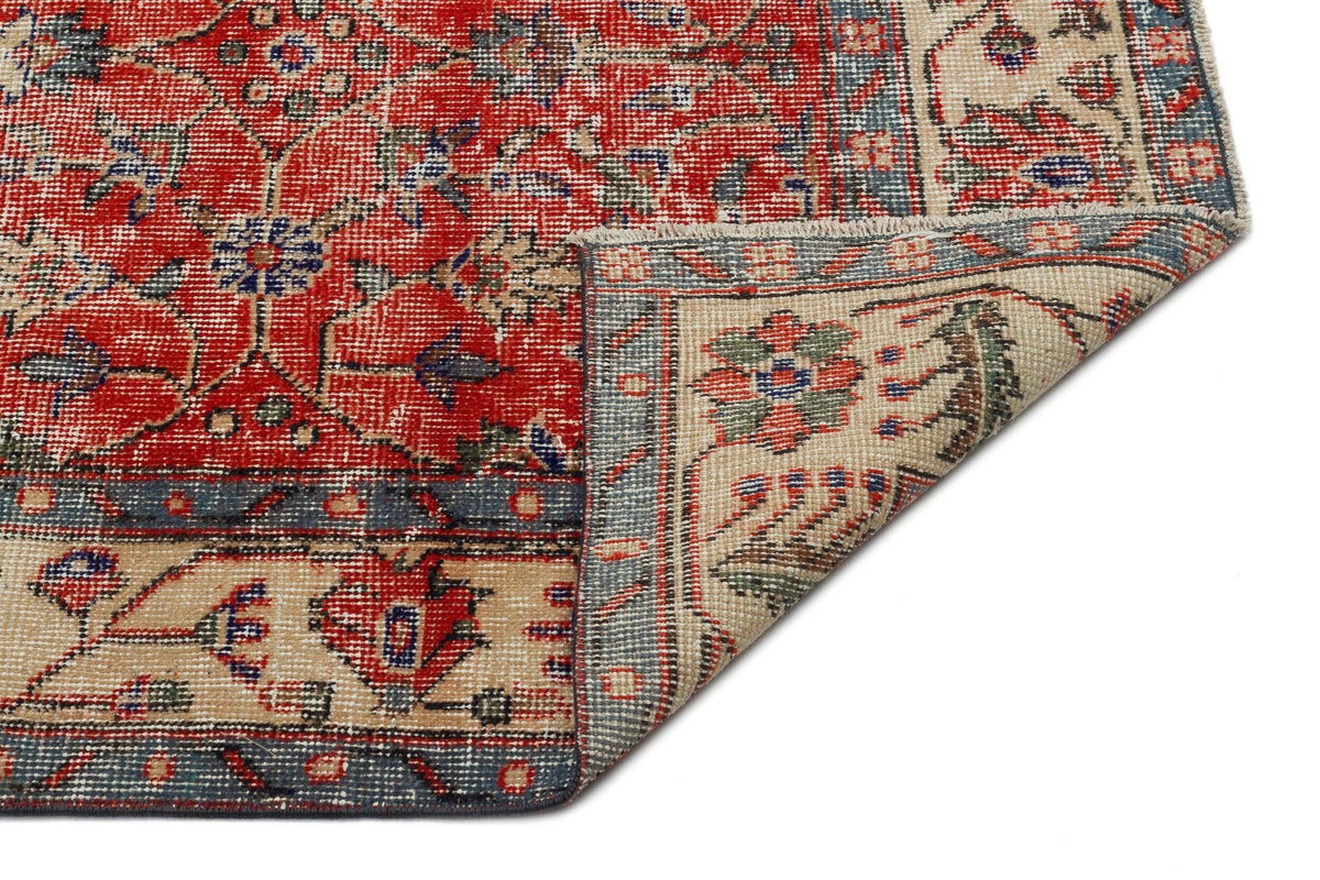 Red, blue, and beige traditional rug with a floral medallion pattern and a folded corner showing the underside.
