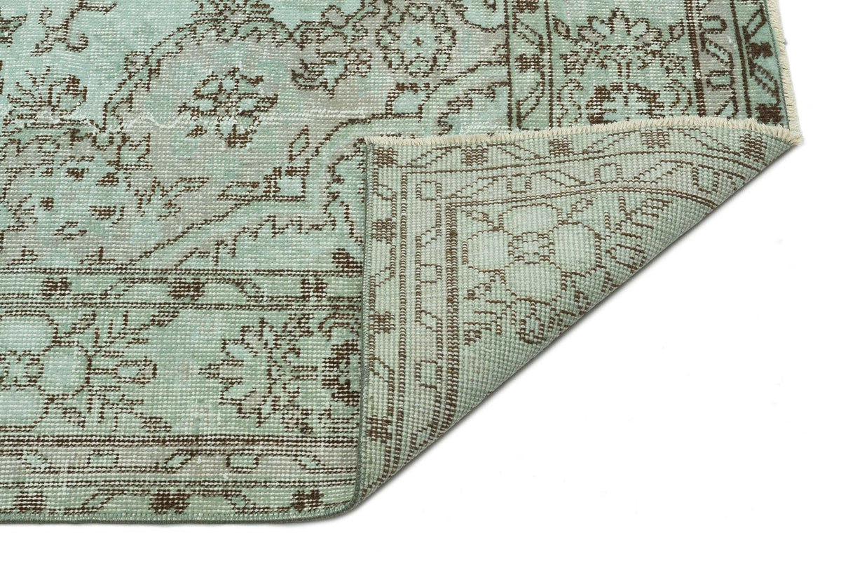 Light blue and brown traditional floral medallion rug with a folded corner on a white background.