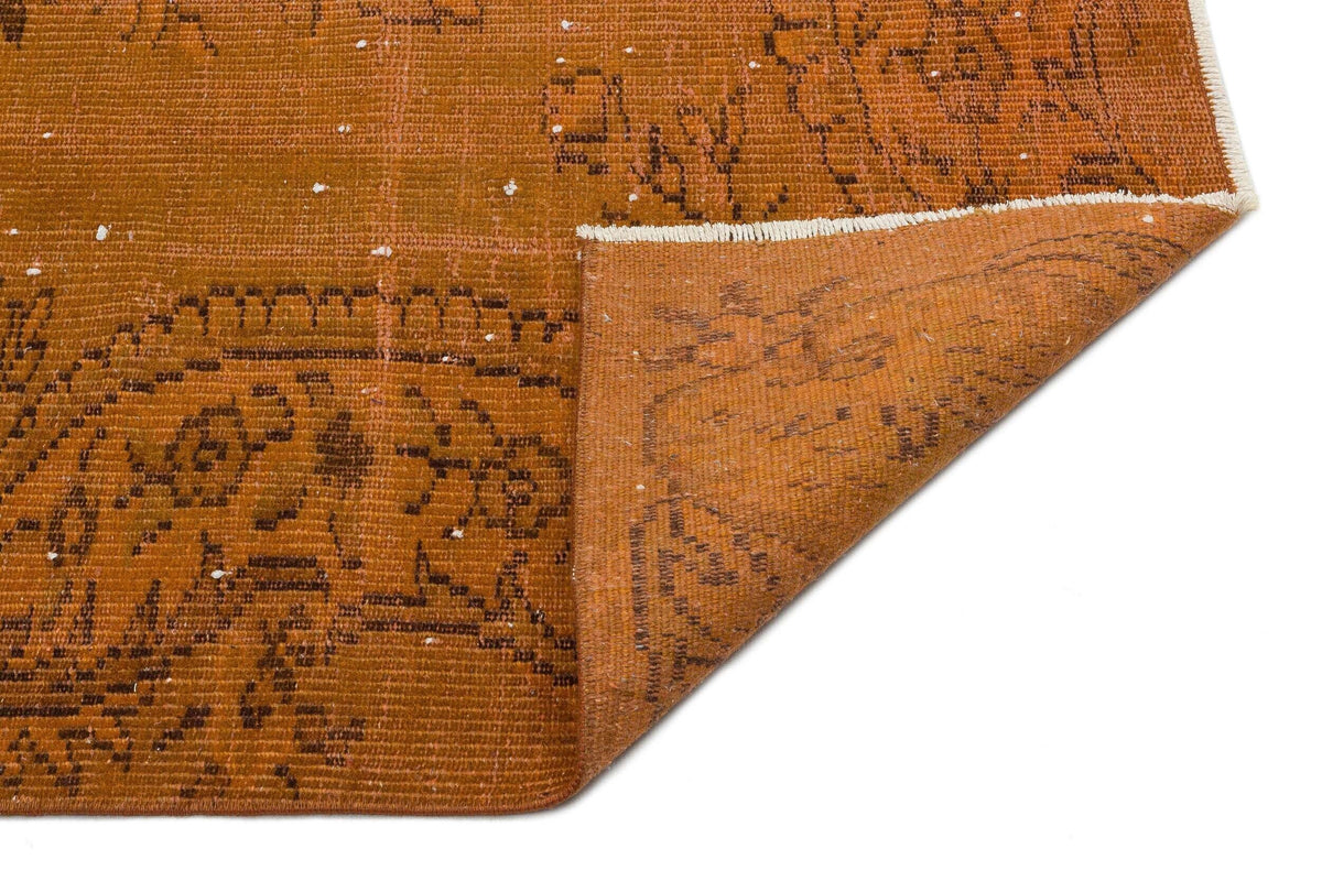 Burnt orange distressed rug with a dark brown traditional medallion pattern and a folded corner on a white background.