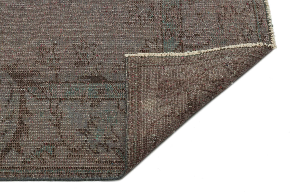 Brown distressed rug with a faded traditional pattern, shown with a corner folded over to reveal the underside.