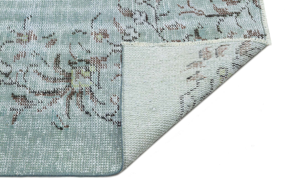 Light blue rug with a distressed floral pattern, shown with a corner folded to reveal the woven backing.