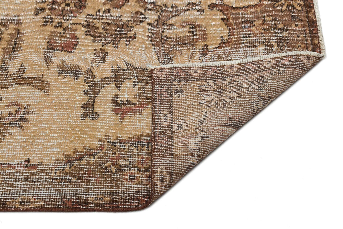 Tan and brown vintage-style rug with a distressed floral medallion pattern, shown with a corner folded over.