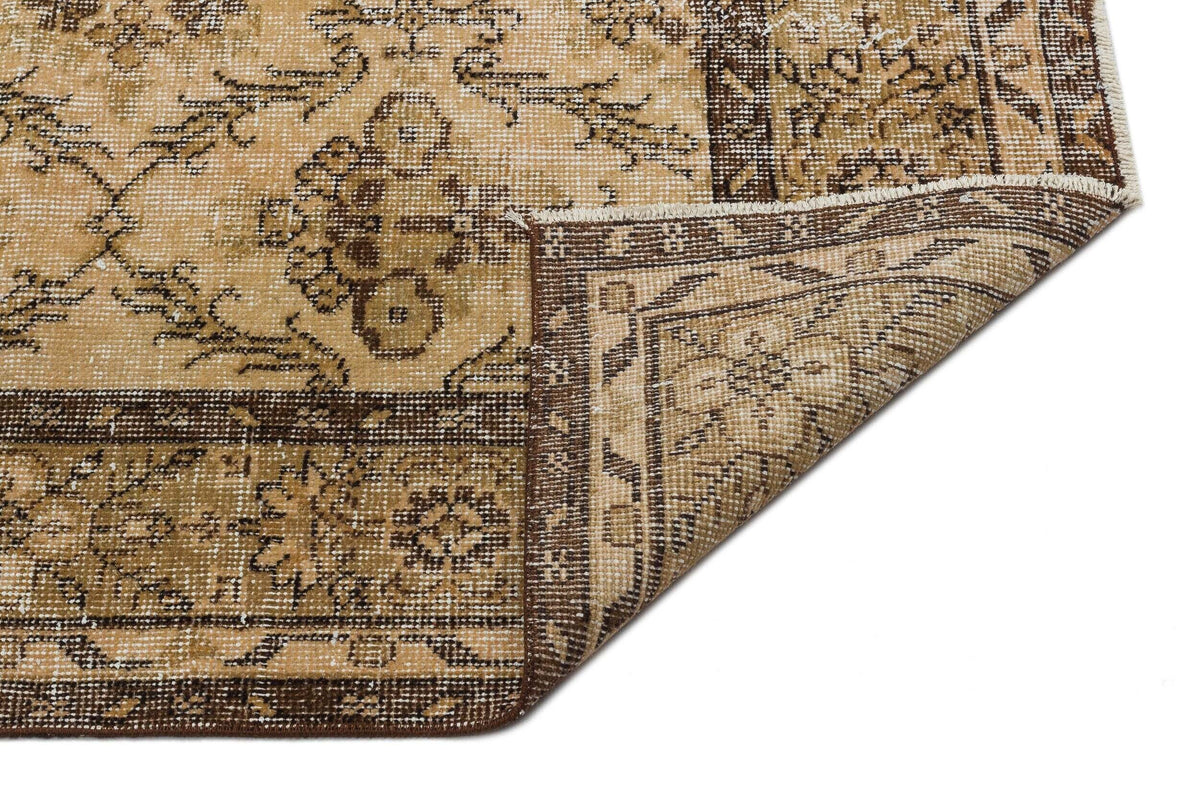 Tan and brown vintage-style rug with a distressed floral medallion pattern and a folded corner, white background.